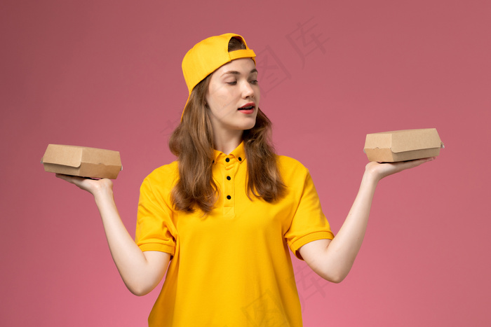 正面图穿着黄色制服和披风的女快递员拿着粉红色墙上的小食品包服务人员送货工作制服