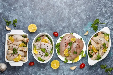 生鸡肉片,大腿,翅膀和腿,香草,香料,柠檬和大蒜在深蓝色背景。俯视图 生鸡肉片,大腿,翅膀和腿,香草,香料,柠檬和大蒜在深蓝色背景。俯视图