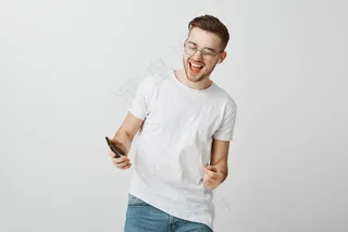 快乐兴奋的家伙微笑着，看着手机，戴着无线耳机跳舞