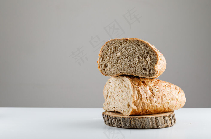 在一张白色的桌子和灰色的表面上的木头上切好的面包。侧视图。文本空间