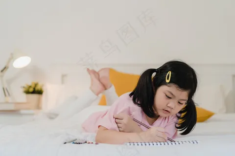 年轻的亚洲女孩在家画画。亚洲日本女人小孩睡前放松休息愉快快乐画漫画躺在床上,晚上在卧室里感受舒适和平静的概念。 年轻的亚洲女孩在家画画。亚洲日本女人小孩睡前放松休息愉快快乐画漫画躺在床上,晚上在卧室里感受舒适和平静的概念。