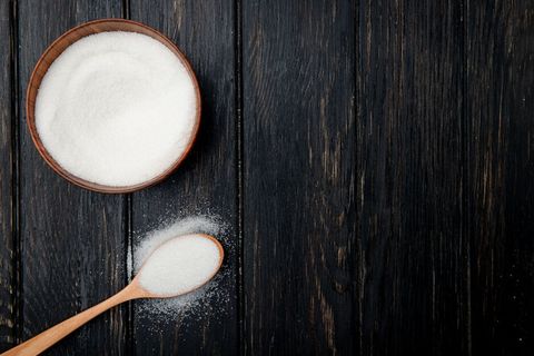 白色砂糖在一个木制碗和一个木制勺子在黑色乡村背景上的顶部视图,带有复制空间 白色砂糖在一个木制碗和一个木制勺子在黑色乡村背景上的顶部视图,带有复制空间