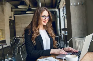 微笑的女商人坐在咖啡馆里用笔记本电脑打字