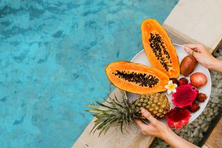 一位女士在泳池边端着一盘美味的热带水果，在豪华酒店吃早餐。