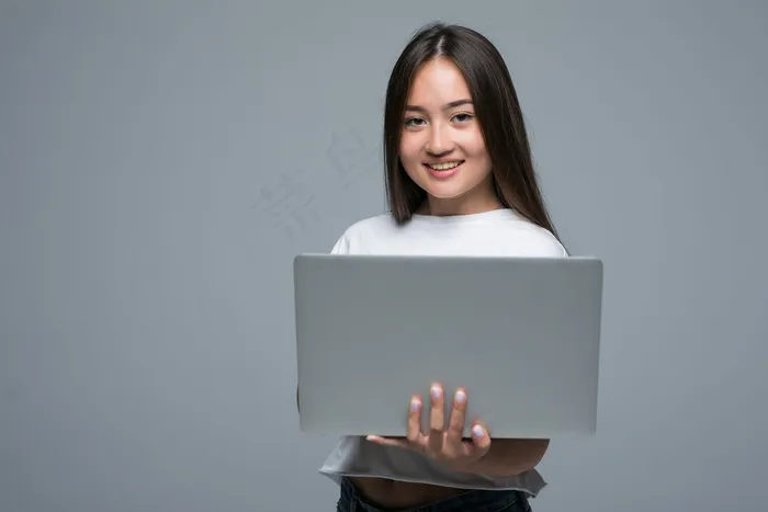 一位亚洲妇女拿着笔记本电脑看着灰色背景的相机