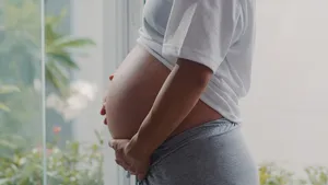 年轻的亚洲孕妇抱着肚子和孩子说话。妈妈开心的笑着积极平和地照顾宝宝，怀孕时在家客厅靠窗的地方。
