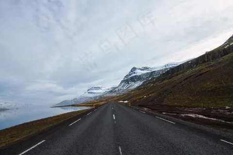 在冰岛多云的天空下,被河流和覆盖着雪和草的小山包围的道路 在冰岛多云的天空下,被河流和覆盖着雪和草的小山包围的道路