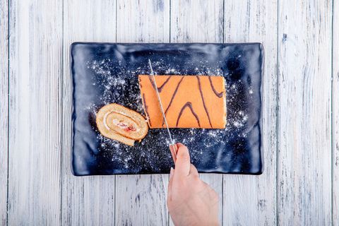 俯视图切一个瑞士卷与生奶油和覆盆子果酱在黑色板上的乡村背景