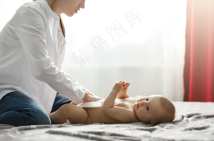 年轻漂亮的母亲穿着白衬衫和牛仔裤，给可爱的新生婴儿铺尿布，准备和爷爷奶奶一起吃家庭晚餐。和家人一起度过特别的时光。