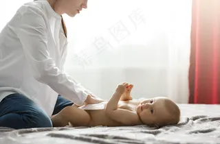 年轻漂亮的母亲穿着白衬衫和牛仔裤，给可爱的新生婴儿铺尿布，准备和爷爷奶奶一起吃家庭晚餐。和家人一起度过特别的时光。