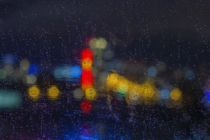 晚上窗户上有雨滴，灯光很亮。抽象的背景，玻璃上的水滴，夜晚的城市灯光。