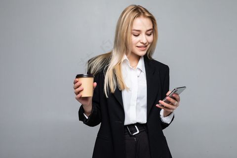 一个满意的年轻女商人拿着一杯咖啡，一边用手机与外界隔绝