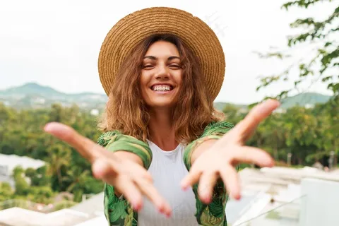 戴着草帽的兴高采烈的女人开心地把手伸向相机。 戴着草帽的兴高采烈的女人开心地把手伸向相机。