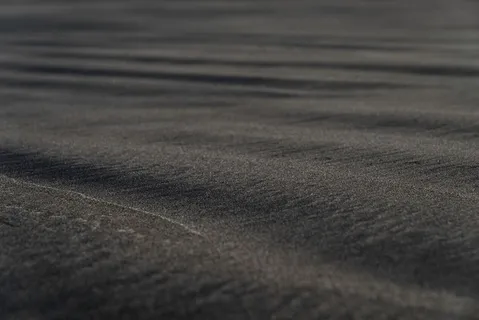 黑沙滩宏观摄影。柔滑的黑色海滩纹理，景深较浅。极简的黑色背景。特内里夫火山砂海岸。