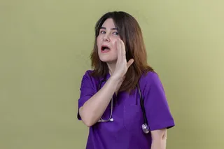 中年女护士穿着制服，手持听诊器，手靠近嘴，站在孤立的绿色背景上讲述秘密