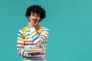 身穿条纹衬衫、背着黄色背包、拿着书、在蓝色墙上思考的男学生正面图