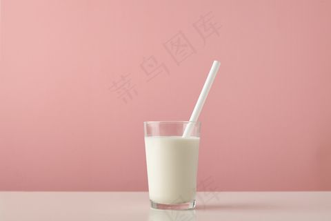 透明玻璃，内有新鲜的有机牛奶和白色吸管，木质桌子上的粉色背景将其隔离