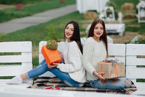 两个美女坐在长椅上，手里拿着礼物