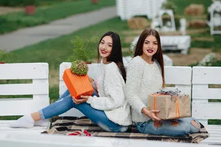 两个美女坐在长椅上，手里拿着礼物