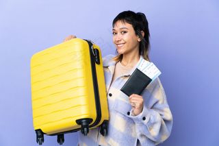 一位年轻的乌拉圭妇女带着旅行箱和护照在紫墙上度假