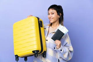 一位年轻的乌拉圭妇女带着旅行箱和护照在紫墙上度假