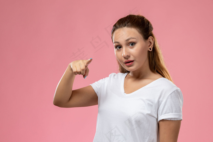 前视图年轻迷人的白色t恤女性，在粉红色的背景上摆出了自己的姿势