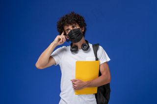 正面图身穿白色t恤的年轻男学生，戴着黑色面具，手持黄色文件，在浅蓝色背景上思考。