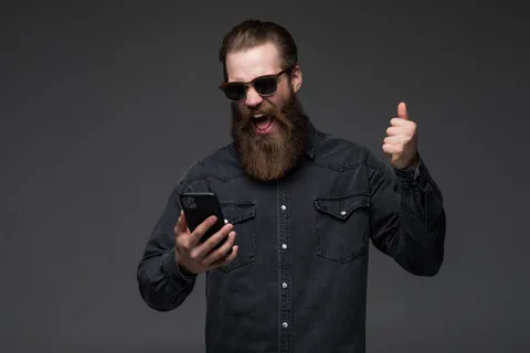 兴奋开朗的男子穿着衬衫用手机庆祝与世隔绝 兴奋开朗的男子穿着衬衫用手机庆祝与世隔绝