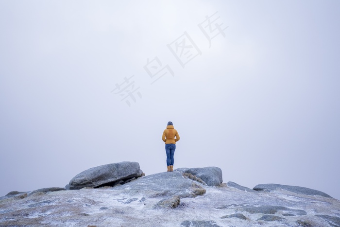 雪山中一位身穿黄色外套的女性站在石头上的美丽照片