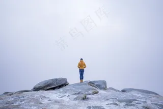 雪山中一位身穿黄色外套的女性站在石头上的美丽照片