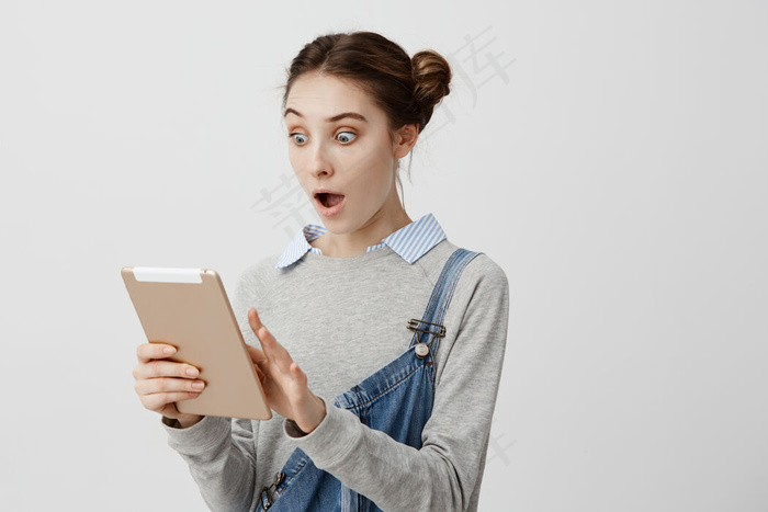 情绪激动的女人张着嘴，瞪着眼睛，在小玩意儿里读着意想不到的信息。黑发女孩，白种人模样，看着笔记本电脑说哇，喜欢它的功能。复制空间