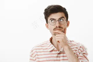 富有创意的聪明办公室经理的肖像，戴着时髦的眼镜，用手摩擦下巴，一边看一边思考或记住重要的公式，在灰色的墙上取得科学突破