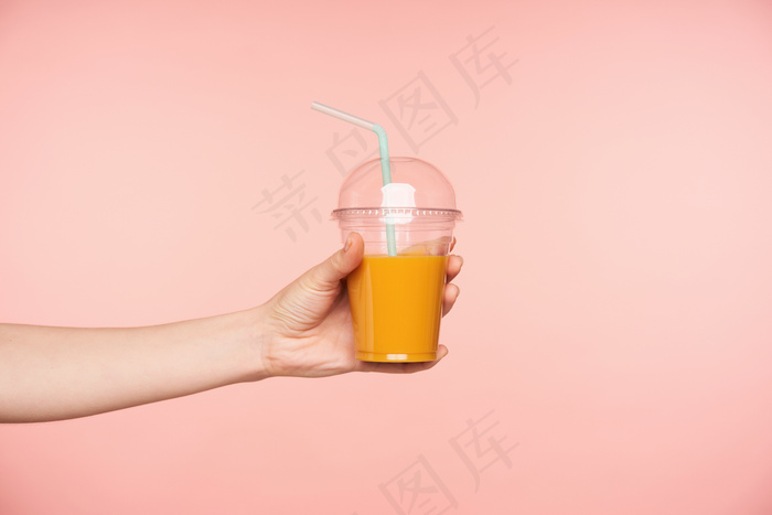 侧视图年轻女子的手被提出，而持有新鲜果汁与吸管在它，隔离在粉红色的背景。餐饮摄影概念