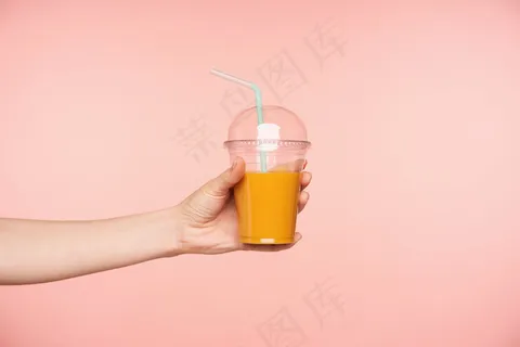 侧视图年轻女子的手被提出，而持有新鲜果汁与吸管在它，隔离在粉红色的背景。餐饮摄影概念