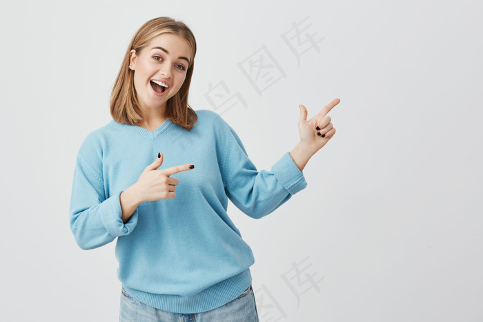 广告概念。一位快乐的年轻欧洲女性，金发碧蓝，站在灰色水泥墙背景下，为您提供信息或宣传内容的复制空间