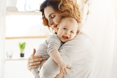 快乐的年轻妈妈抱着宝贝孩子,轻轻地抱着他的小身体。孩子开心地笑着,用灰色的大眼睛看着摄像机。 快乐的年轻妈妈抱着宝贝孩子,轻轻地抱着他的小身体。孩子开心地笑着,用灰色的大眼睛看着摄像机。
