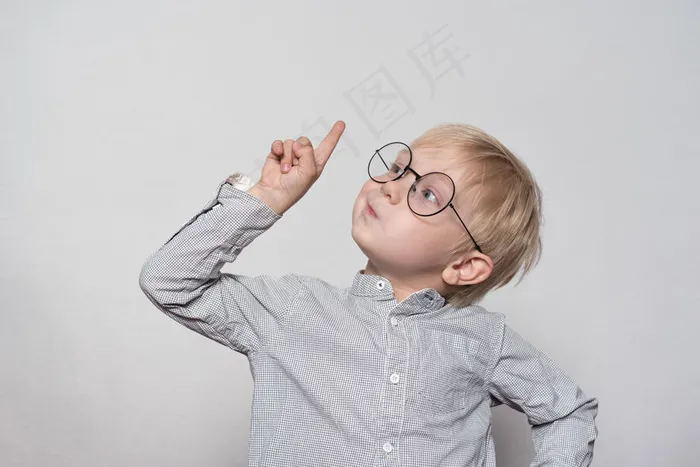 一个戴着大眼镜的金发男孩的画像。手指向上。