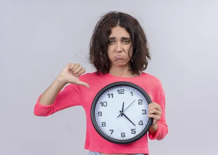 一个年轻漂亮的女孩拿着时钟,拇指朝下,在一个白色的背景和复印空间 一个年轻漂亮的女孩拿着时钟,拇指朝下,在一个白色的背景和复印空间