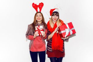 两个微笑的女人拿着新年礼物。戴着可爱的化妆帽。坦率的微笑。庆祝心情。闪光肖像。