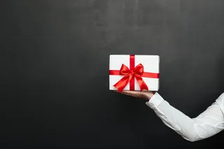 不规则的男性手拿白色礼物盒，红色蝴蝶结，隔离在深灰色的墙上