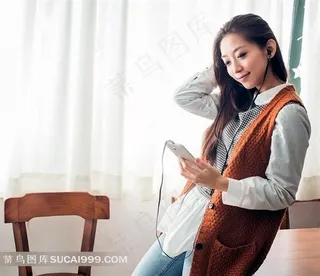 窗帘前手拿手机听歌曲靠在桌子上的女孩