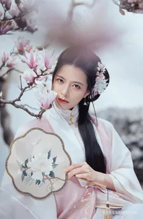 手拿传统刺绣牡丹锦绣扇在木兰花旁的粉色古装女子图片