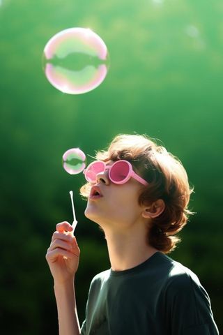 小孩吹泡泡玩耍绿叶背景