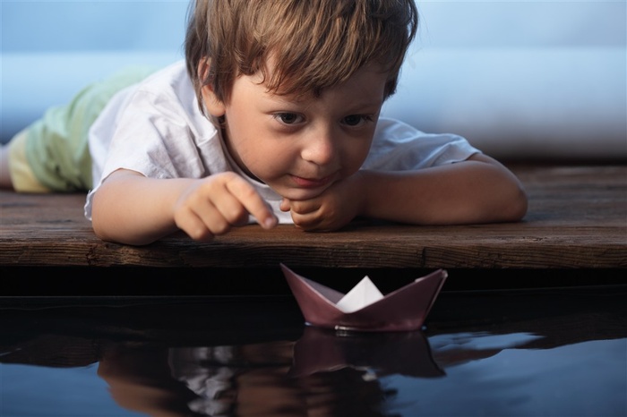 水面木板上玩纸船的小男孩高清图片