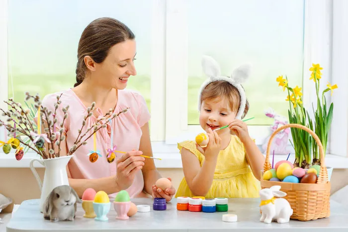 一个母亲和她的女儿画复活节彩蛋，可爱的小女孩戴着小兔子耳朵。