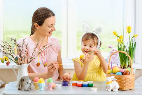 一个母亲和她的女儿画复活节彩蛋，可爱的小女孩戴着小兔子耳朵。