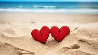 海边沙滩上摆放着两个红色爱心互相依靠摄影图