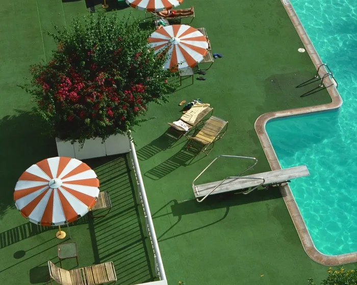 游泳池边草地上旱伞下的躺椅