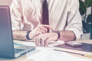 坐在办公桌前看手表的商务人士