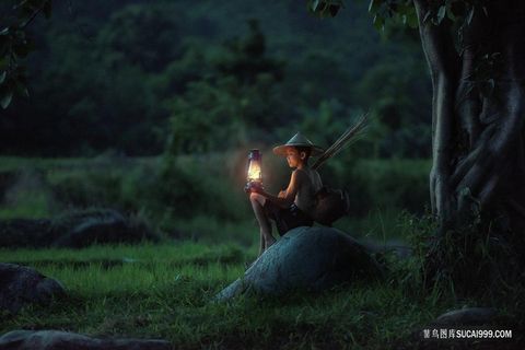 夜晚树下点着煤油灯的小男孩